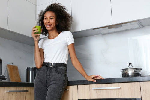 Happy woman drinking a green smoothie in the kitchen